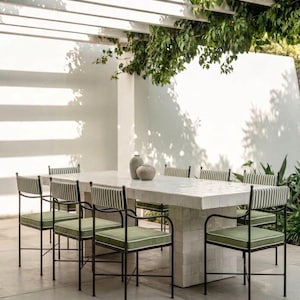 Puede incluir: Una mesa de comedor rectangular con superficie de azulejos blancos y base de pedestal a juego, rodeada de seis sillas de metal negro con cojines y respaldos de tela a rayas verdes y blancas, con dos jarrones grises redondeados sobre la mesa.