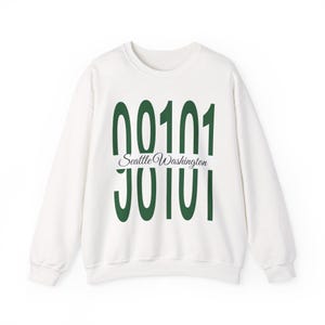 Op de afbeelding: Een wit sweatshirt met lange mouwen en een ronde hals, voorzien van grote, donkergroene verticale cijfers 98101, met de tekst Seattle Washington in een kleiner, zwart cursief lettertype horizontaal over het midden van de cijfers.
