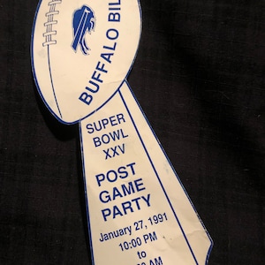 May include: White paper ticket shaped like a football trophy with blue text and a blue buffalo logo. The text reads "Buffalo Bills Super Bowl XXV Post Game Party January 27, 1991 10:00 PM to 2:00 AM 0811 Admit One Only".