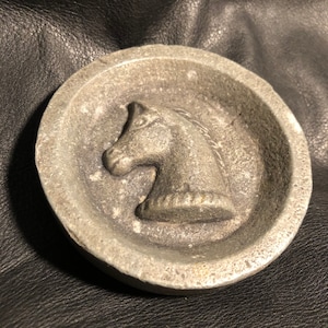 May include: A silver metal ashtray with a raised horse head design.