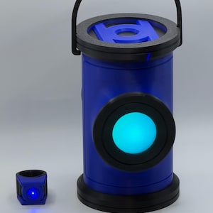 May include: A blue cylindrical lantern with a black handle and a glowing cyan circular light on the front, featuring a blue lantern symbol on top. Beside it sits a small blue ring with a tiny, bright blue LED light embedded in the center.