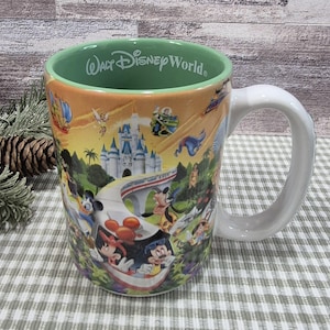 May include: A ceramic mug with a white handle and a colorful wrap-around design featuring Disney characters and the text "Walt Disney World." The interior rim is green. The mug showcases iconic Disney imagery.