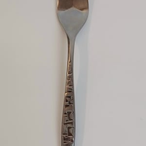 May include: A stainless steel fork with three tines. The handle features a textured, geometric pattern. The fork is designed for eating and is a common utensil for meals. The fork is approximately 8 inches long.