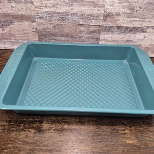 Puede incluir: Una bandeja rectangular turquesa para hornear con un patrón de diamantes en la base. La bandeja tiene lados ligeramente curvos y asas en cada extremo. Está hecha de un material duradero y está diseñada para hornear.