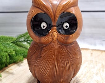 May include: A brown ceramic owl figurine with large black eyes and white pupils. The owl has detailed feather textures and is perched on a brown base. The figurine is a decorative item.