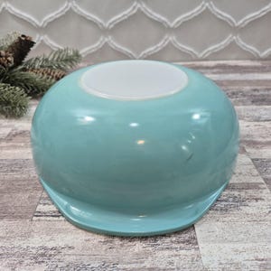 May include: A vintage turquoise blue mixing bowl made of milk glass. The bowl features a smooth, rounded body with a wide, flat base and a slightly flared rim. The exterior has a glossy finish, and the interior base is a solid white color.