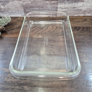 May include: A rectangular clear glass baking dish with rounded corners and a smooth rim. The center of the base features embossed text that reads: Pyrex, Made in USA, 233, 3 QT, 2.8 L, For Oven and Microwave, No Stovetop or Broiler.