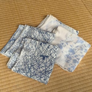 May include: Two folded square fabric cloths with blue and white patterns. One cloth features a dense, dark blue crisscross line design on a white background, while the other displays a soft, light blue floral print on a white fabric base.