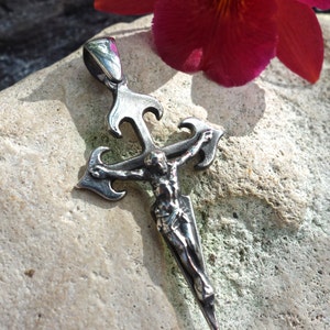 May include: A silver pendant in the shape of a crucifix with a detailed figure of Jesus Christ. The pendant is on a gray stone background.