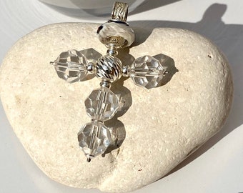 May include: A silver cross pendant with clear crystal beads. The cross is made of sterling silver and features a detailed design. The pendant is resting on a white stone.