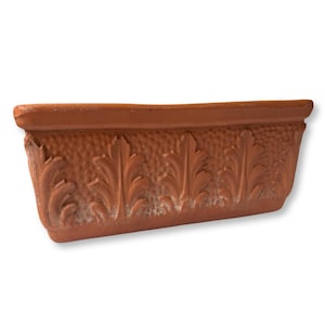 May include: A rectangular terracotta planter featuring a repeating embossed leaf pattern along the front side. The surface has a textured, stippled finish between the raised foliage designs, and the material has a natural reddish-brown clay color.