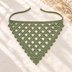 May include: A sage green triangular bandana featuring an intricate openwork crochet pattern with a scalloped edge and two long ties at the top corners. The accessory is crafted with a repeating diamond-shaped lattice design throughout the body.