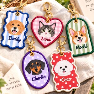 Puede incluir: Cinco llaveros bordados con cierres de mosquetón dorados. Las formas incluyen un rectángulo de rayas azules con Buddy, un corazón de cuadros rosas con Luna, un arco de rayas verdes con Mochi, un óvalo de lunares morados con Charlie y una forma festoneada de lunares rojos con Coco.