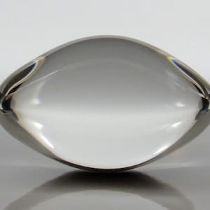May include: A clear glass paperweight shaped like a football. The paperweight is smooth and reflective.