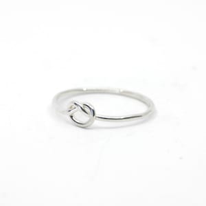 May include: A silver knot ring with a simple design. The ring is thin and delicate, and the knot is smooth and polished.