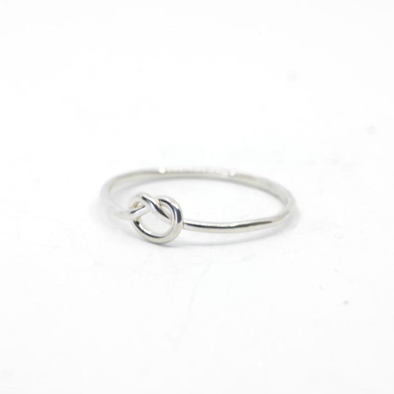 May include: A silver knot ring with a simple design. The ring is thin and delicate, and the knot is smooth and polished.
