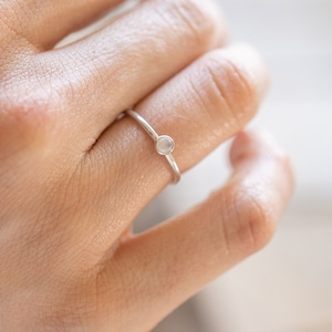 Puede incluir: Un anillo de plata con una pequeña piedra redonda blanca.