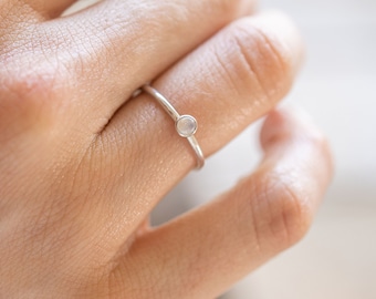 May include: A silver ring with a small, round, white gemstone.