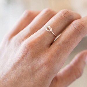 May include: A silver knot ring on a finger.