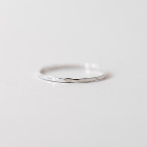 May include: A thin silver band ring with a hammered texture.