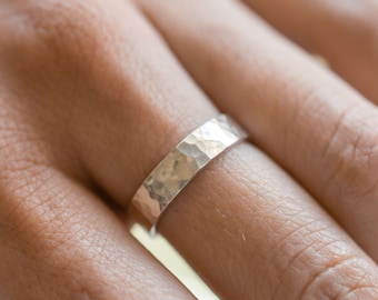 May include: A silver hammered band ring worn on a finger.