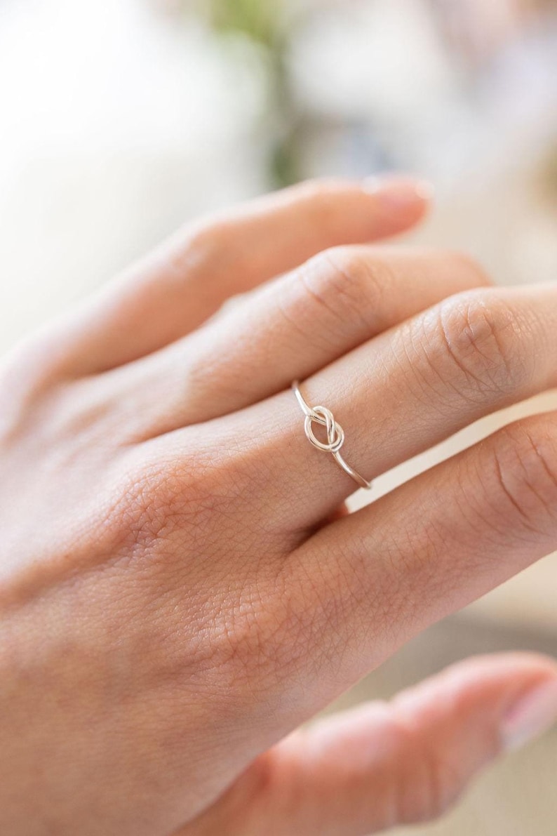 May include: A silver knot ring on a finger.
