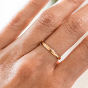 May include: A gold-colored ring with a smooth, rounded band. The ring is shown on a person's finger, with the focus on the ring's polished surface. The ring appears to be a simple, classic design, suitable for everyday wear.