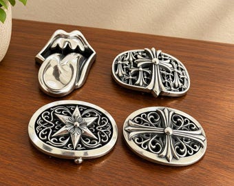 May include: Four silver-toned metal belt buckles. One is shaped like a mouth with a tongue, one is an oval with a central cross and smaller cross motifs, one is an oval with a six-pointed star, and one is an oval with a large ornate cross.