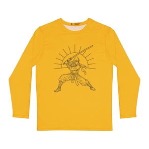 May include: A long-sleeve yellow shirt featuring a black line art graphic of a ninja in a combat stance holding a sword, positioned in front of a rising sun design. The shirt has a crew neckline and a size L label printed on the inner collar.