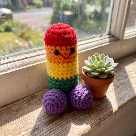 A handmade crochet penis with a positive attitude — tiny yarn desk buddy that somehow nails 'emotional support' as a gag gift concept.
