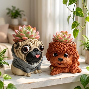 May include: Two animal-shaped planters, one a beige pug wearing a gray hoodie and the other a brown curly-haired poodle, each holding a green and pink succulent plant on top of their heads, positioned side by side on a white wooden surface.
