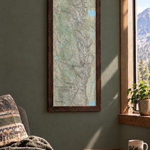 May include: A vertical wall map of The Sierra Nevada encased in a dark, textured wooden frame. The map displays detailed topographical terrain, blue lakes, and a compass rose. The text reads The Sierra Nevada, Sequoia & Kings Canyon, Yosemite, Wilderness, and High Sierra.