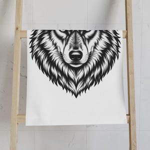 May include: A white rectangular towel featuring a high-contrast black ink illustration of a wolf head centred on the fabric. The graphic depicts the detailed facial features, sharp eyes, and thick fur of the wolf in a stylised, bold line art.