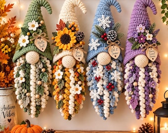 May include: Four hanging crochet gnome decorations with pointed hats, each featuring unique seasonal embellishments like flowers, pinecones, and snowflakes. Each gnome has a wooden heart tag with text reading Hello Fall, Bee Kind, Let it Snow, and Home Sweet Home.