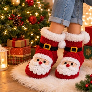 May include: A pair of red and white crochet slippers designed to look like Santa Claus, featuring a black belt with a yellow buckle, a white fluffy cuff, and a detailed face with a beard, mustache, and red nose on the front of each slipper.