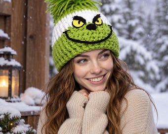 May include: A lime green and white crocheted beanie featuring a large lime green yarn pom-pom on top. The hat displays a character face with yellow eyes, black pupils, and a wide black stitched smile across the front of the green section.