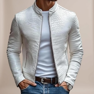 May include: A white jacket featuring a textured crocodile skin pattern, a stand-up collar, and a full-length silver zip closure. The garment is worn over a plain white t-shirt, paired with blue denim jeans and a brown leather belt with a silver buckle.