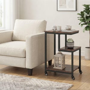 May include: A three-tier side table with a black metal frame and dark wood-grain shelves. The table features a C-shaped design with four small caster wheels at the base, providing mobility for the unit while holding various decorative items.