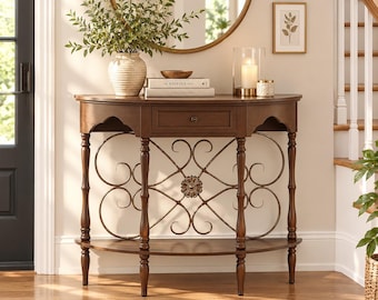 May include: A semi-circular wooden console table with a single drawer, featuring four turned legs and a lower shelf. The front includes decorative metal scrollwork with a central floral medallion. A textured vase, books, and a candle sit on top.
