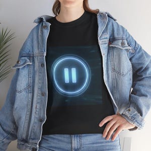 May include: A black t-shirt featuring a glowing blue circular pause icon with two vertical bars in the center, worn under a light blue denim jacket with metal buttons and a classic collar, paired with matching light blue denim jeans.