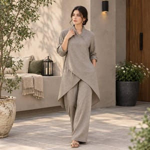 May include: A taupe-colored two-piece set consisting of a long-sleeved tunic with a wrap-style front, a V-neckline, and an asymmetrical hemline, paired with matching wide-leg trousers. The garment features a textured fabric finish throughout.