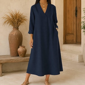 May include: A long-sleeved, ankle-length navy blue dress featuring a V-neckline and a loose, flowing silhouette. The garment has a simple, solid-colored design with cuffed sleeves and a straight hemline, providing a clean and uniform appearance.
