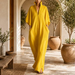 Könnte beinhalten: Ein senfgelbes Maxikleid mit lockerer Passform, einem strukturierten Kragen und weiten Kimono-Ärmeln. Das Kleidungsstück verfügt über einen tiefen V-Ausschnitt und Seitentaschen und ist aus einem strukturierten Stoff gefertigt, der bis zum Boden reicht.