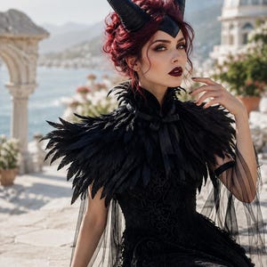 May include: A black feathered shoulder cape with a high collar and ribbon tie, worn over a black lace dress. The ensemble includes a black headpiece featuring two large, curved horns and a dark forehead accent, paired with sheer black arm sleeves.