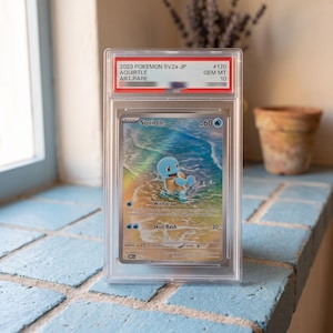 May include: A graded 2023 Pokemon SV2a JP Squirtle Art Rare trading card in a clear plastic slab. The card features a blue Squirtle character standing in shallow ocean water on a sandy beach. The label at the top reads 2023 POKEMON SV2a JP #170.