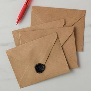 Pode incluir: Uma pilha de quatro envelopes de papel castanho com um selo de cera preto no envelope superior.