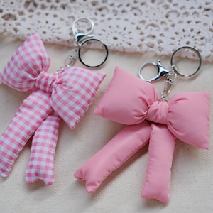 May include: Two pink bow keyrings. One bow is made of checked fabric and the other is made of a smooth fabric.