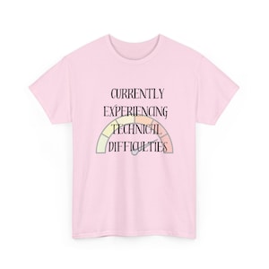Op de afbeelding: Een lichtroze T-shirt met korte mouwen en een afbeelding van een meter met de tekst "CURRENTLY EXPERIENCING TECHNICAL DIFFICULTIES" in het zwart gedrukt. De meter heeft segmenten in lichtgroen, geel, oranje en lichtrood.
