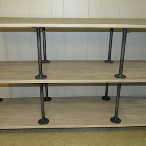 May include: A three-tiered rolling shelf unit with a whitewashed wood top and black metal pipe frame. The shelf has wheels and two handles.