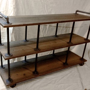 May include: A three-tiered industrial-style shelf unit with a wooden top and black metal pipe frame. The shelf has a rustic brown finish and features a metal handle on the top shelf.